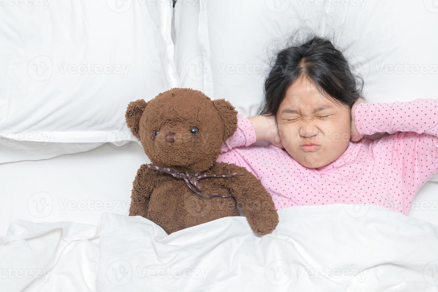 pequeño niña cubierta orejas postergación molesto ruidoso ruido, tapones orejas a evitar escuchando sonido en cama. foto
