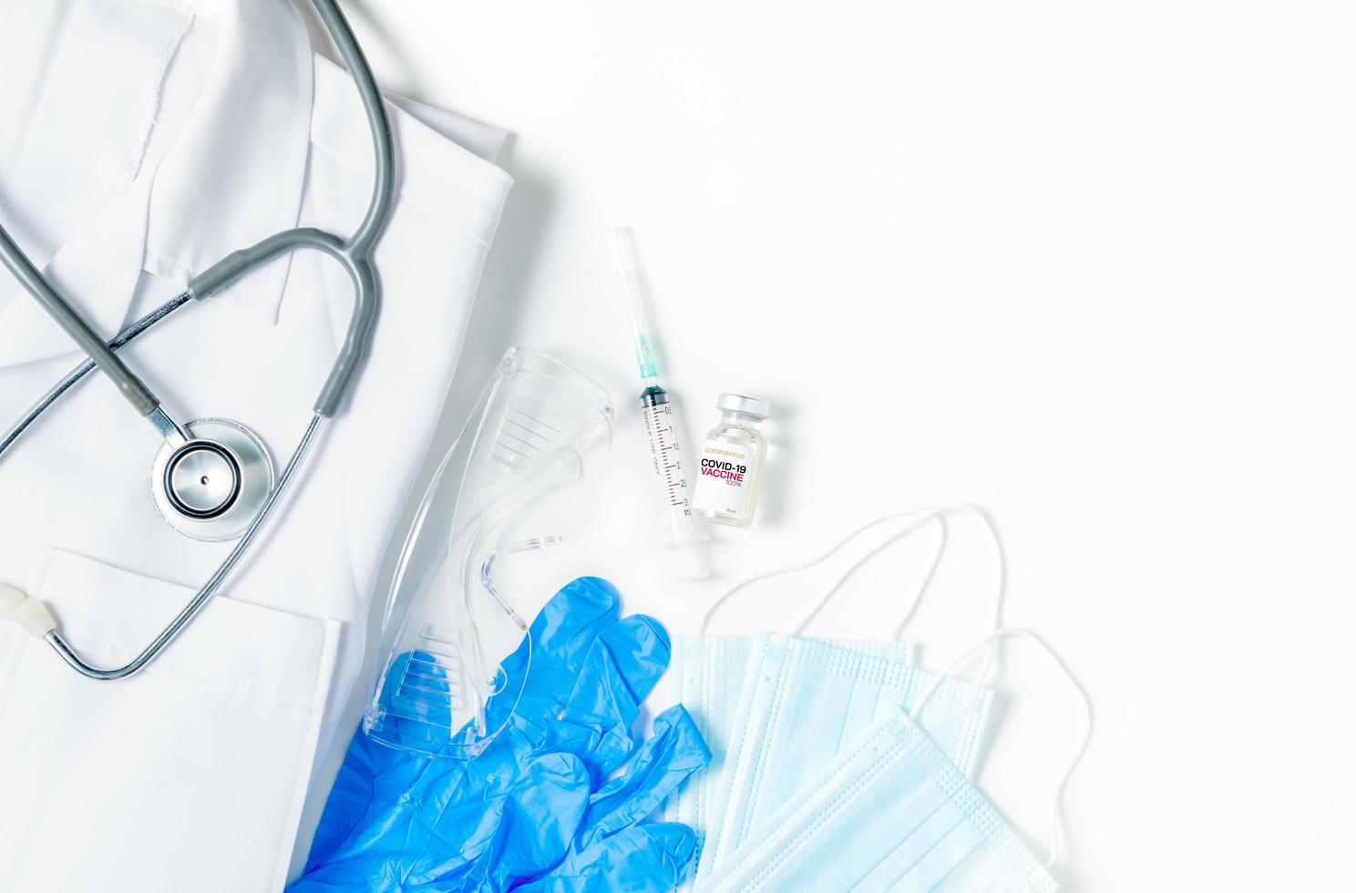 A vial of the Covid 19 vaccine with syringe and stethoscope on gown shirt isolated photo
