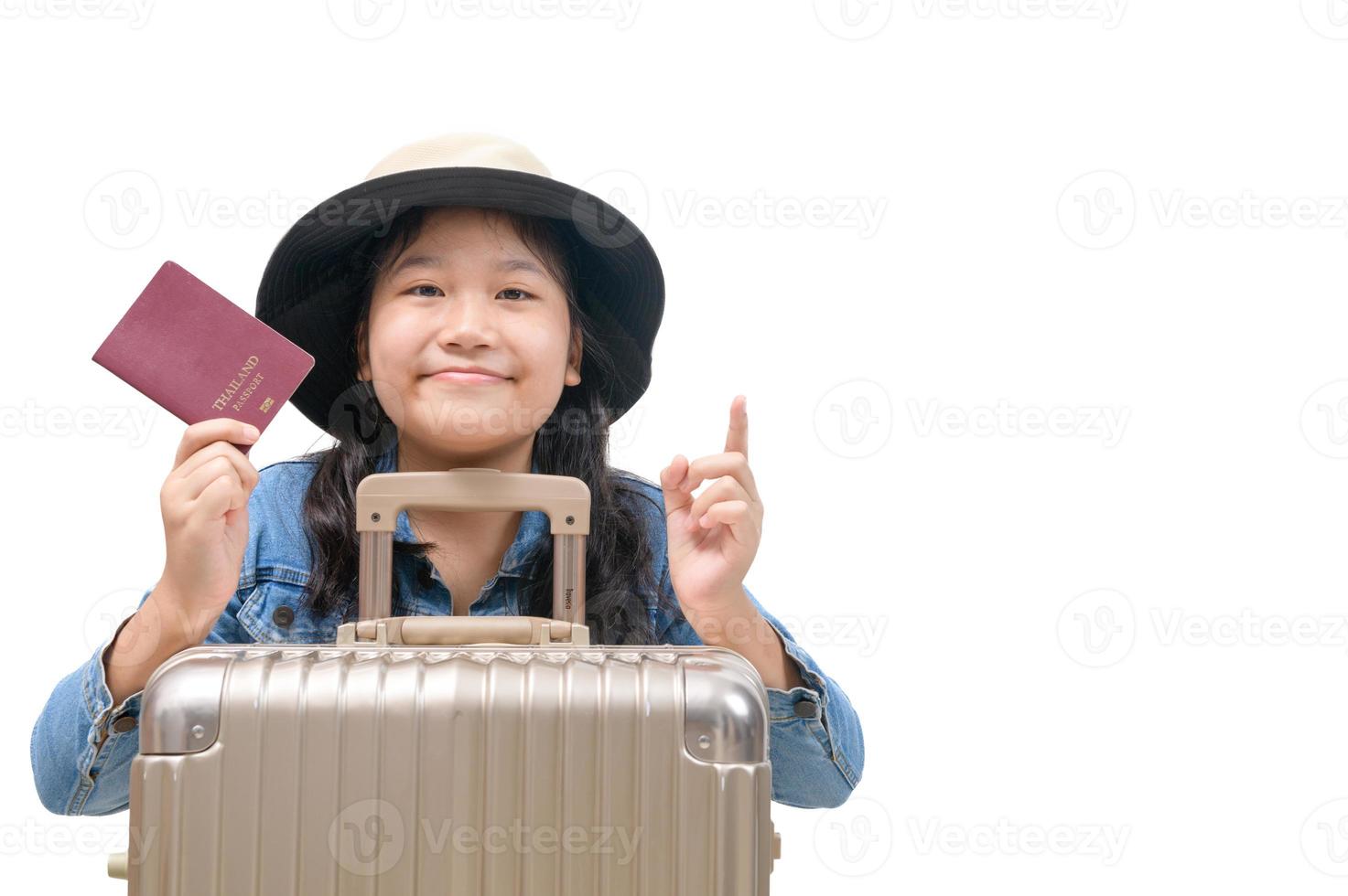 Cute asian kid ready to travel wearing a hat and holding her passport with luggage isolated photo