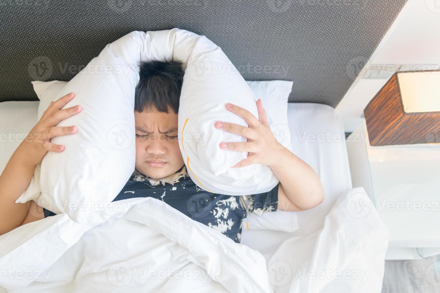obeso chico acostado en cama cubierta cabeza con almohada porque también ruidoso molesto ruido. yo foto