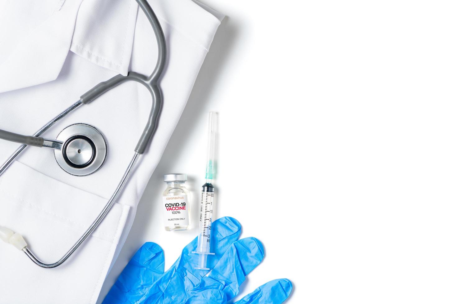 A vial of the Covid 19 vaccine with syringe and stethoscope on gown shirt isolated on white background, photo