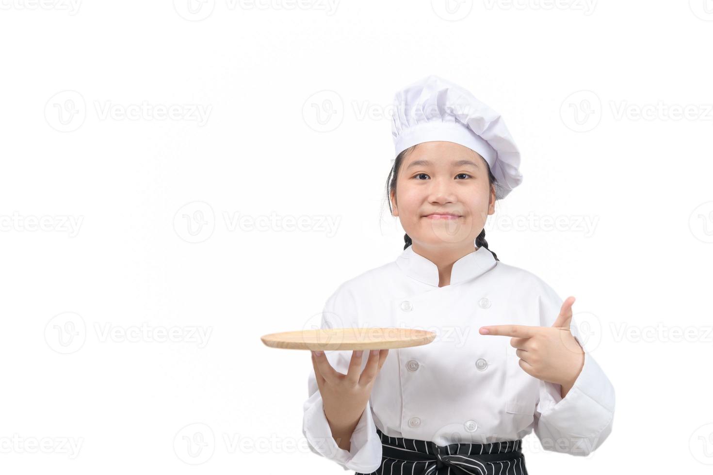 cute girl chef holds wooden plate and points her finger at plate. food menu presentation photo