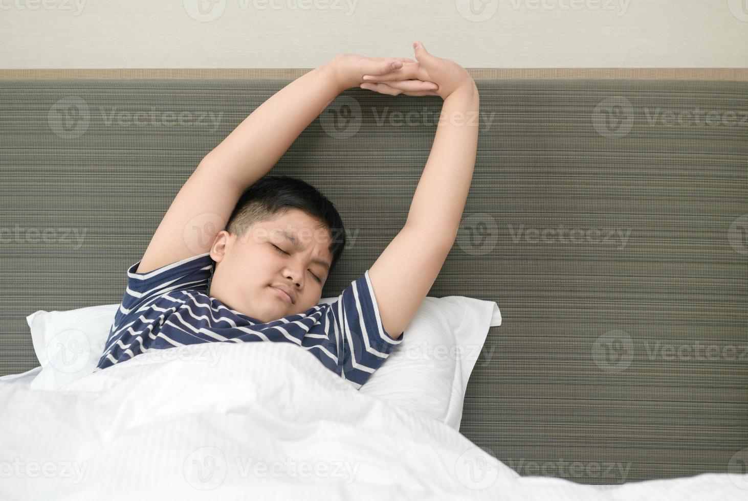 obese fat boy wakes up and stretching on bed in morning, photo
