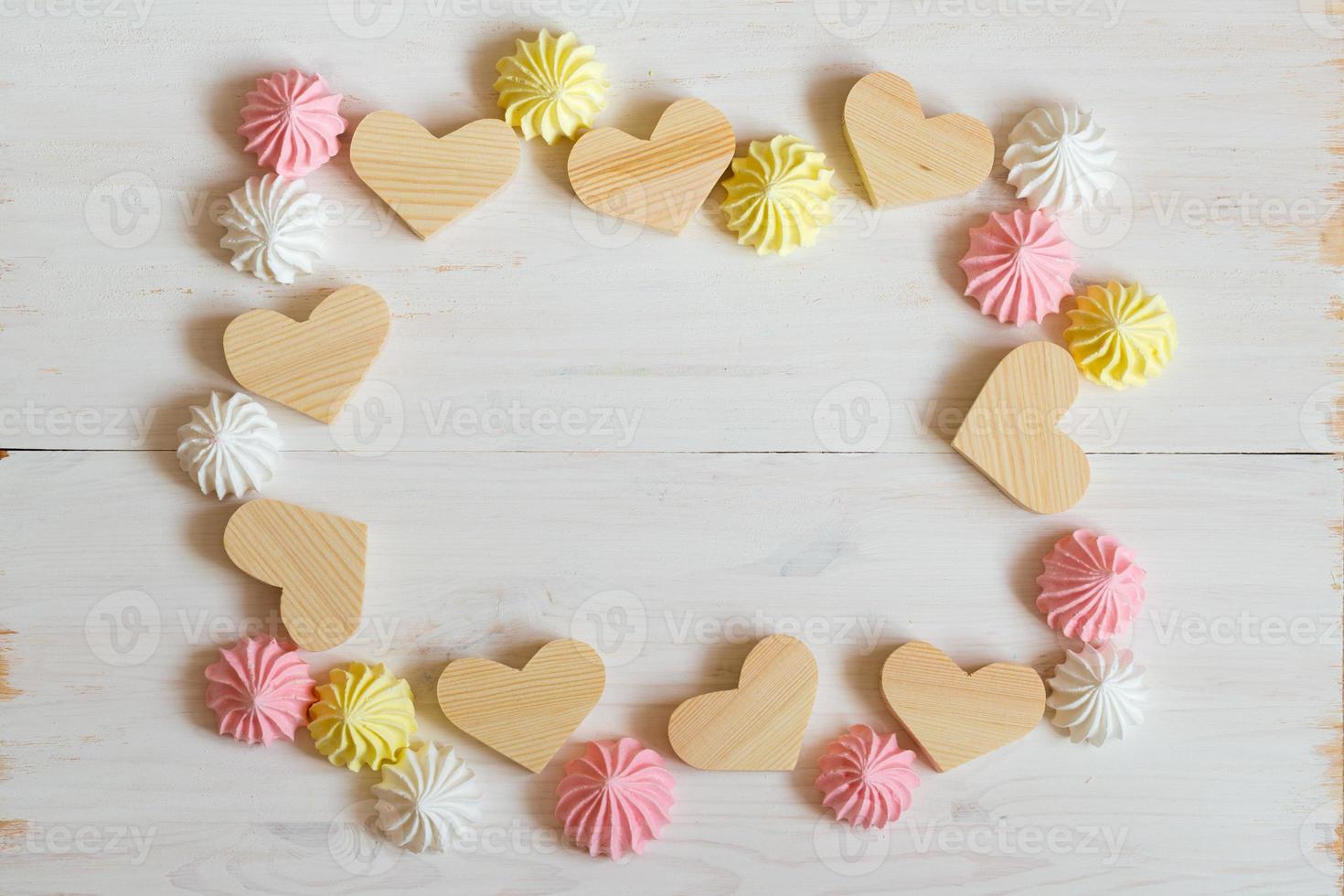 Frame made of wooden hearts and meringue pastel colors on a white wooden background photo