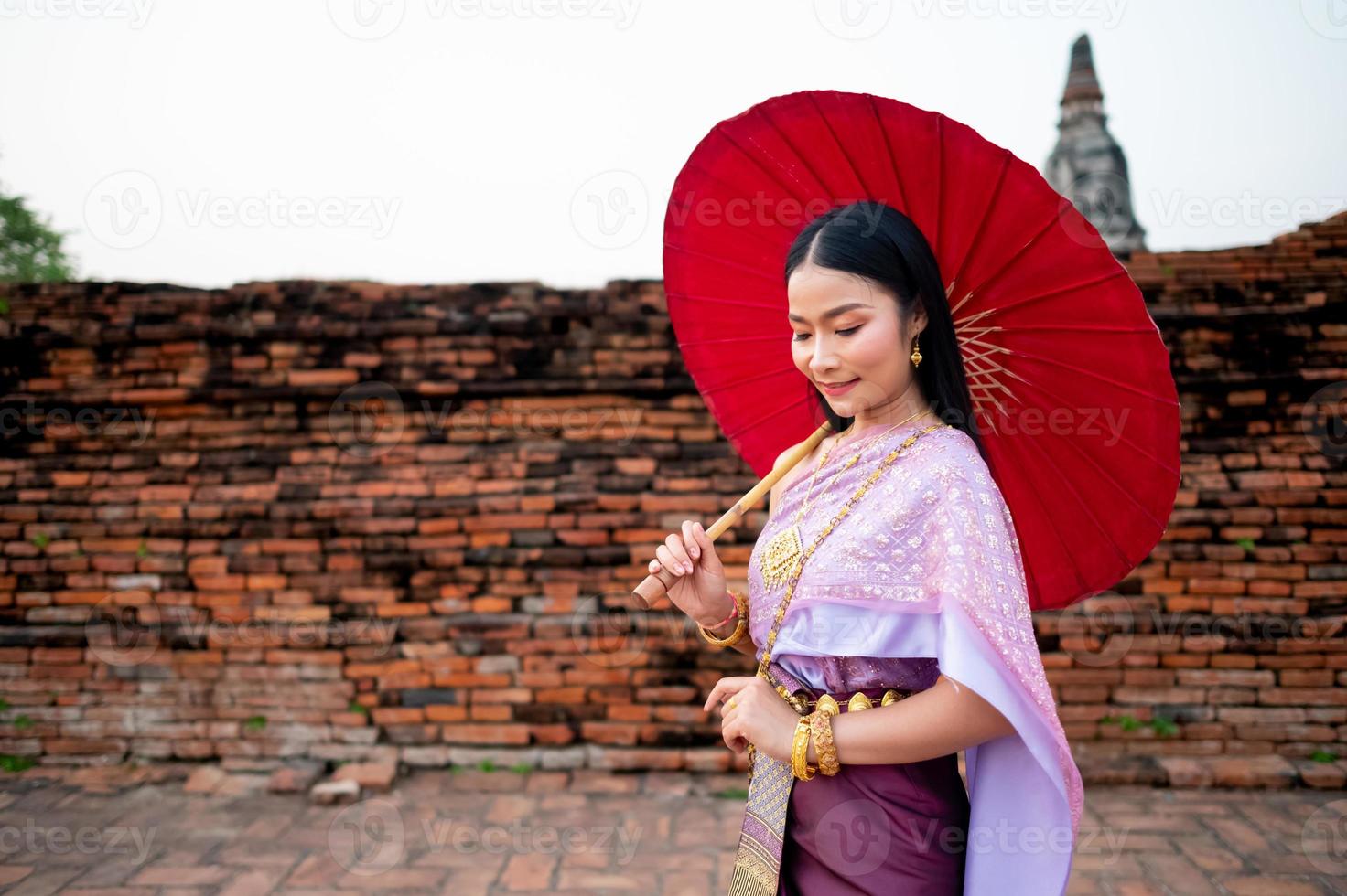 Beautiful Thai girl in traditional dress costume red umbrella as Thai temple where is the public place, Thai Woman in Traditional Costume of Thailand. photo