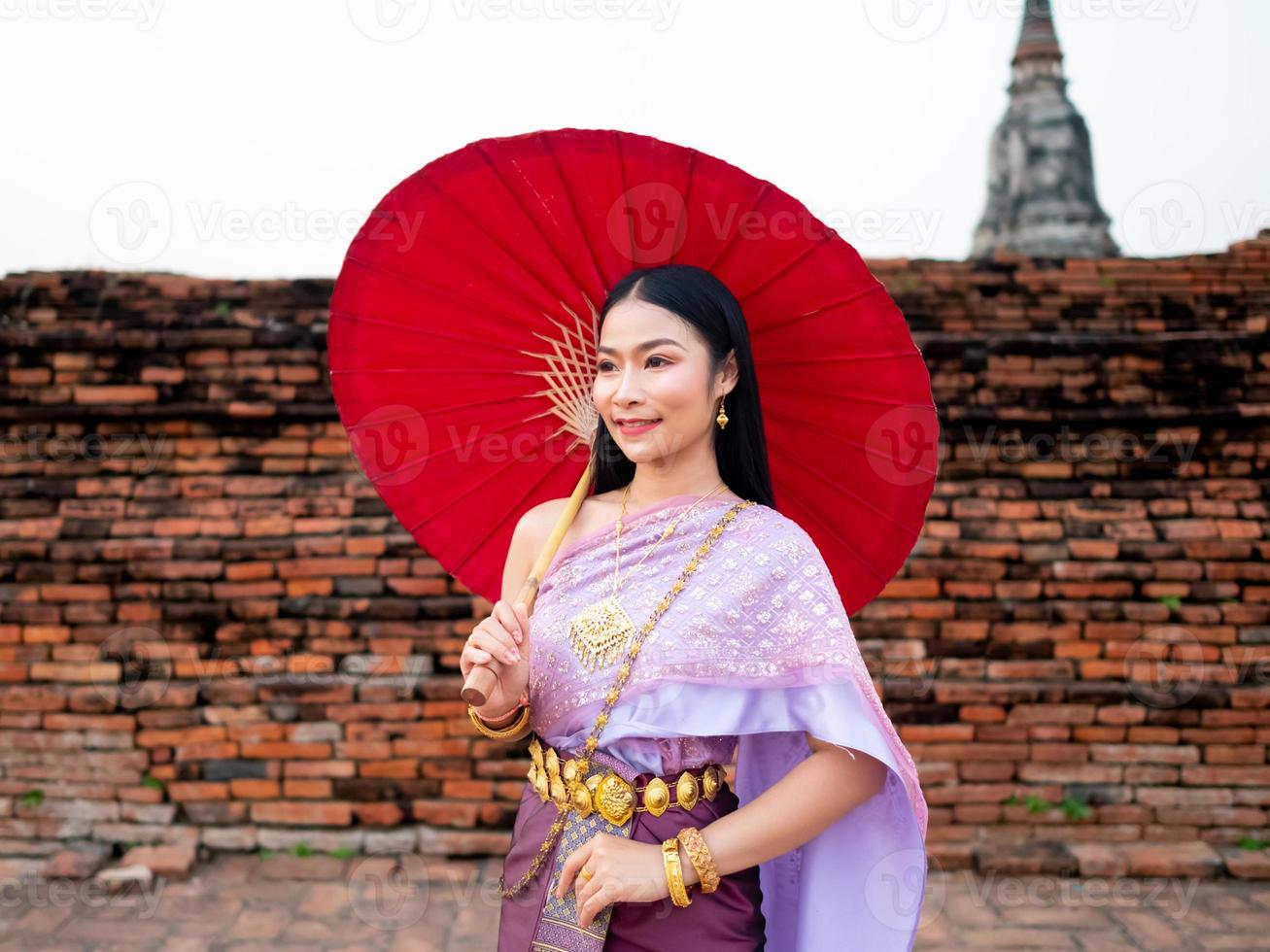 Beautiful Thai girl in traditional dress costume red umbrella as Thai temple where is the public place, Thai Woman in Traditional Costume of Thailand. photo