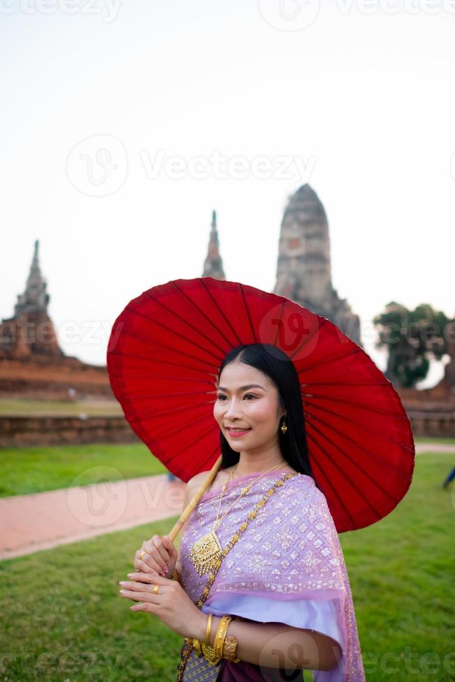 Beautiful Thai girl in traditional dress costume red umbrella as Thai temple where is the public place, Thai Woman in Traditional Costume of Thailand. photo