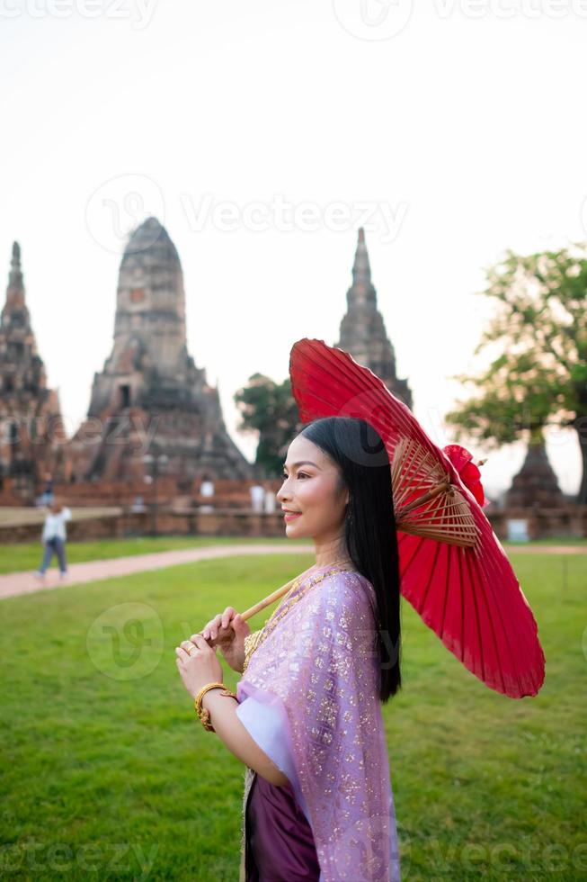 hermosa tailandés niña en tradicional vestir disfraz rojo paraguas como tailandés templo dónde es el público lugar, tailandés mujer en tradicional disfraz de tailandia foto