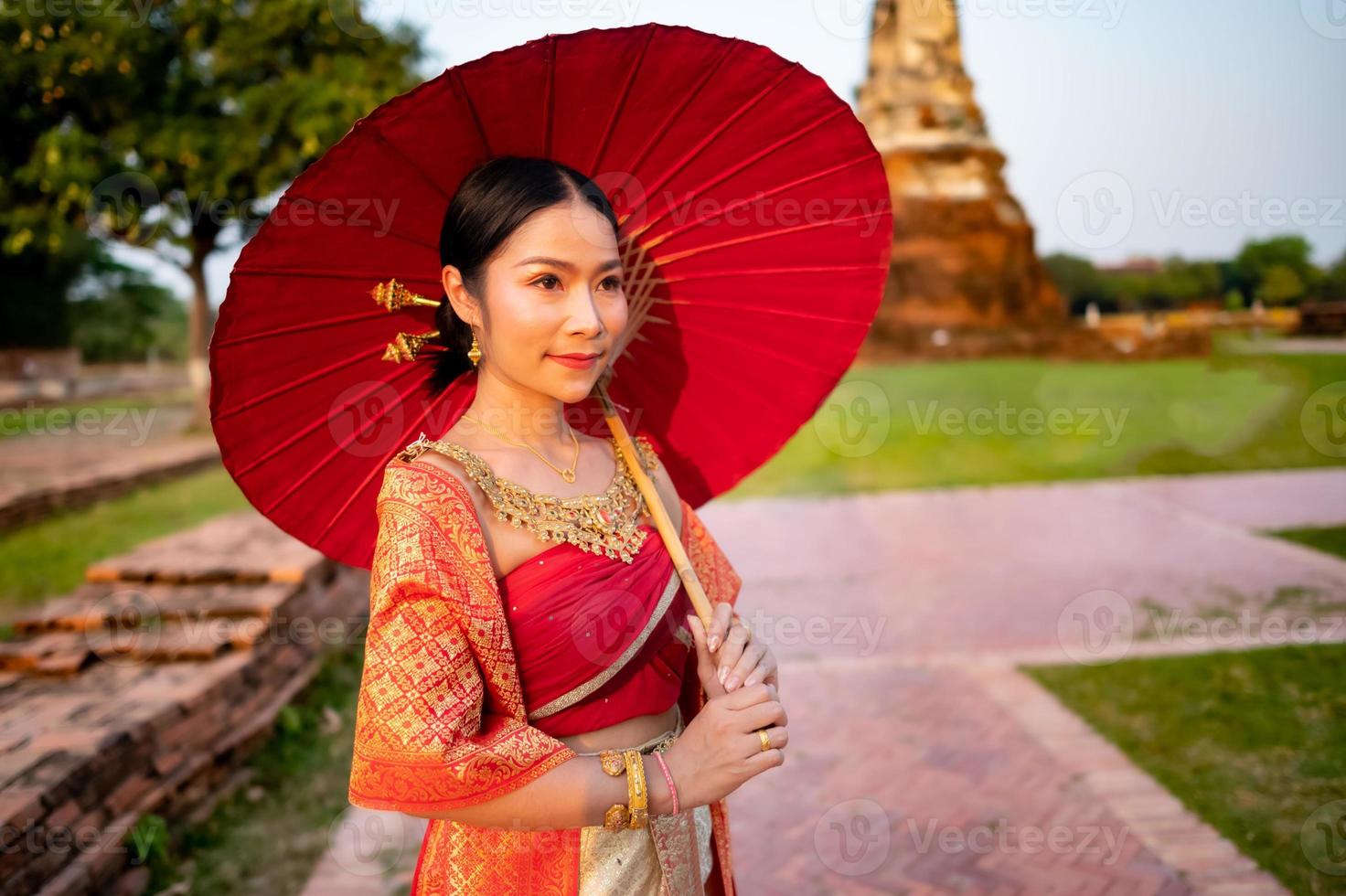 Beautiful Thai girl in traditional dress costume red umbrella as Thai temple where is the public place, Thai Woman in Traditional Costume of Thailand. photo
