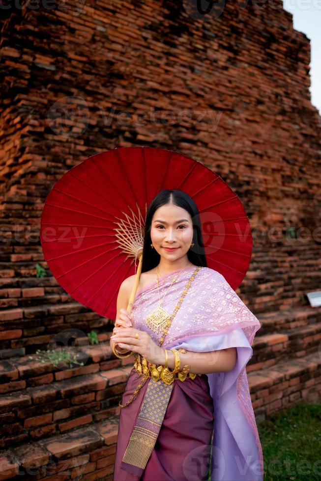 hermosa tailandés niña en tradicional vestir disfraz rojo paraguas como tailandés templo dónde es el público lugar, tailandés mujer en tradicional disfraz de tailandia foto