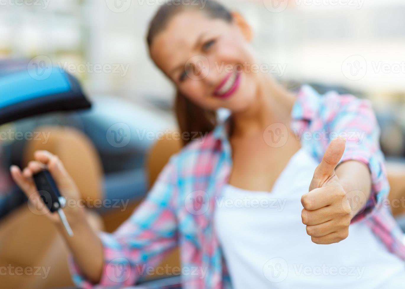 joven contento mujer en pie cerca un convertible con el llaves en su mano y pulgar arriba foto