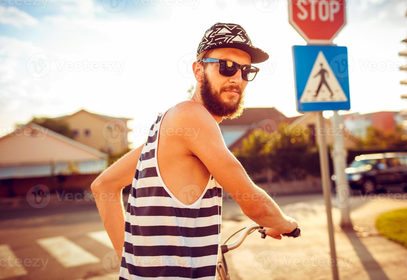 Young man in sunglasses riding a bicycle on a city street at sunset light photo