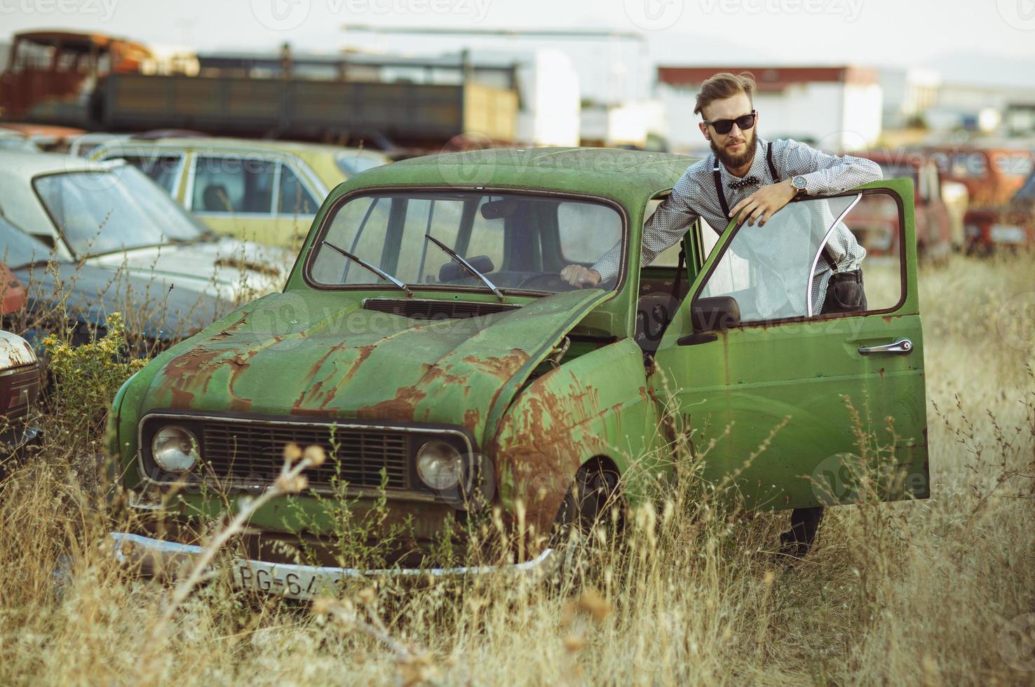 Young stylish handsome man, wearing shirt and sunglasses, driving old car photo