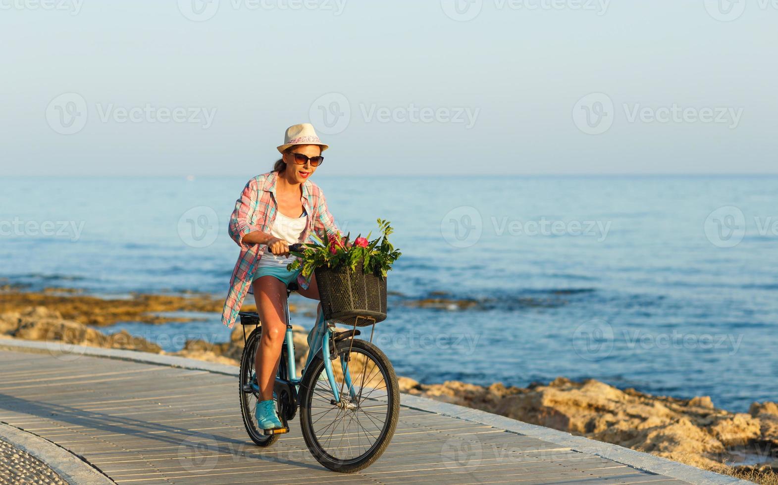 Carefree woman with bicycle riding on a wooden path at the sea, having fun and smiling photo