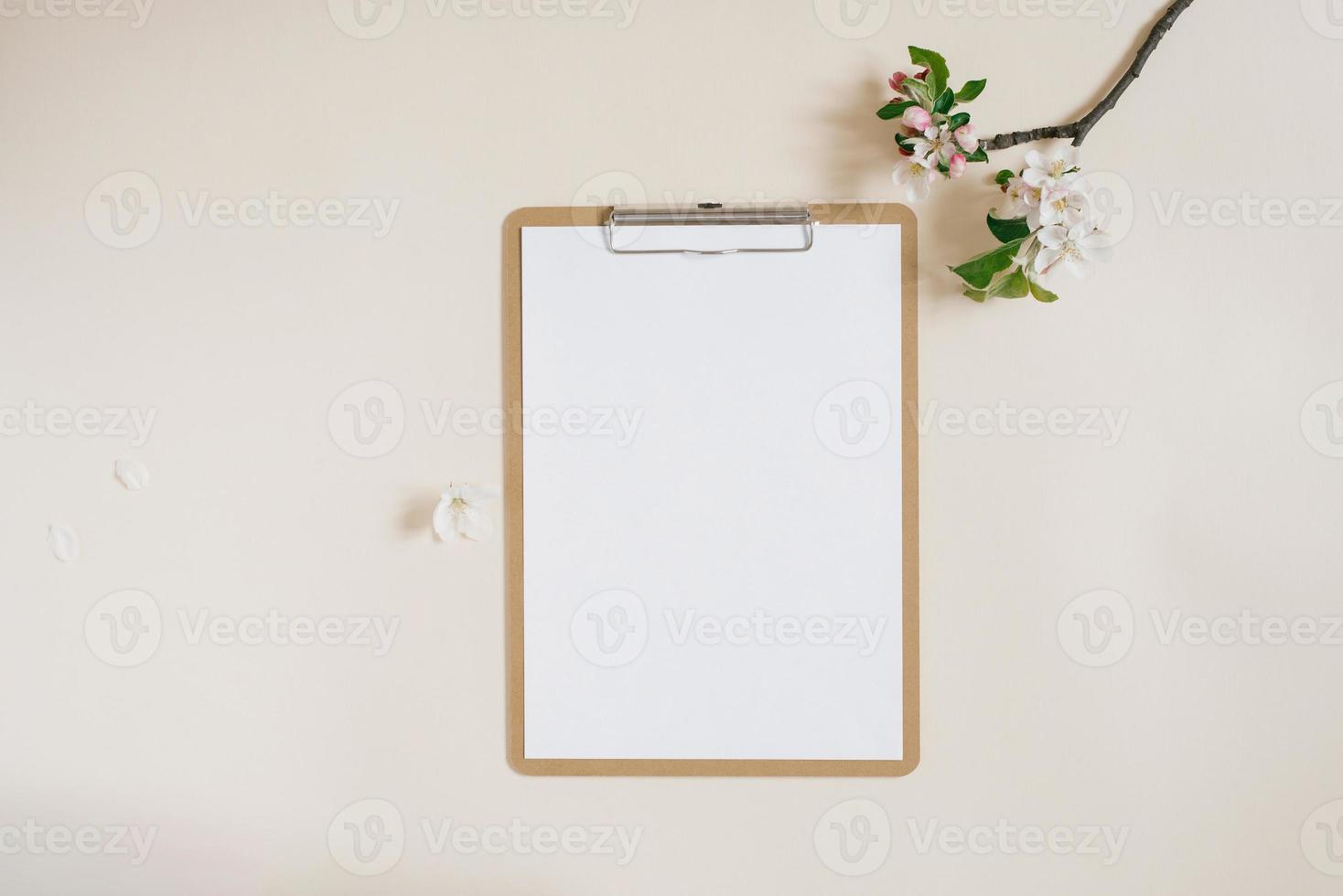 Workspace with clipboard and branch of apple tree with flowers on beige background flat lay photo