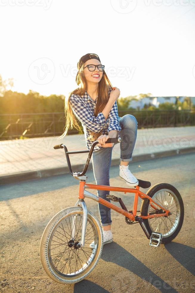 Lovely young woman in a hat riding a bicycle on city background in the sunlight outdoor photo