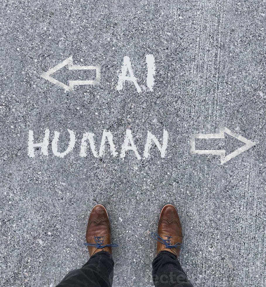 Man looking down at the words Artificial Intelligence - AI - and Human chalked onto the floor photo