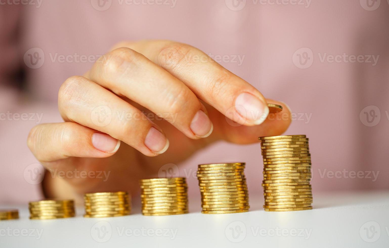 Female hand stacking gold coins into increasing columns photo
