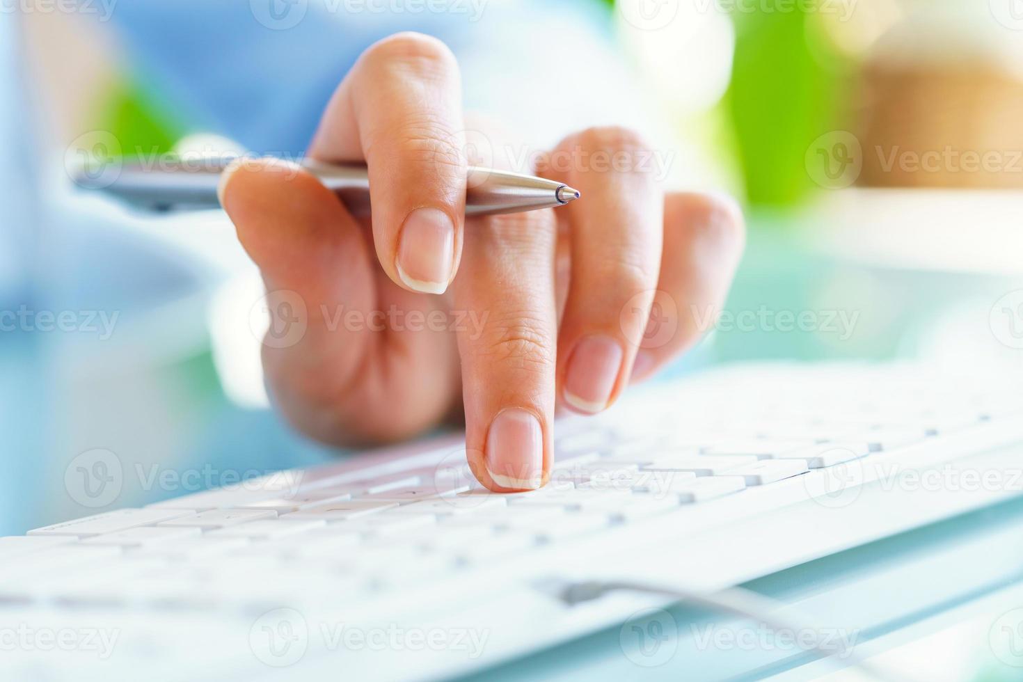 Woman office worker with pen in hand typing on the keyboard photo