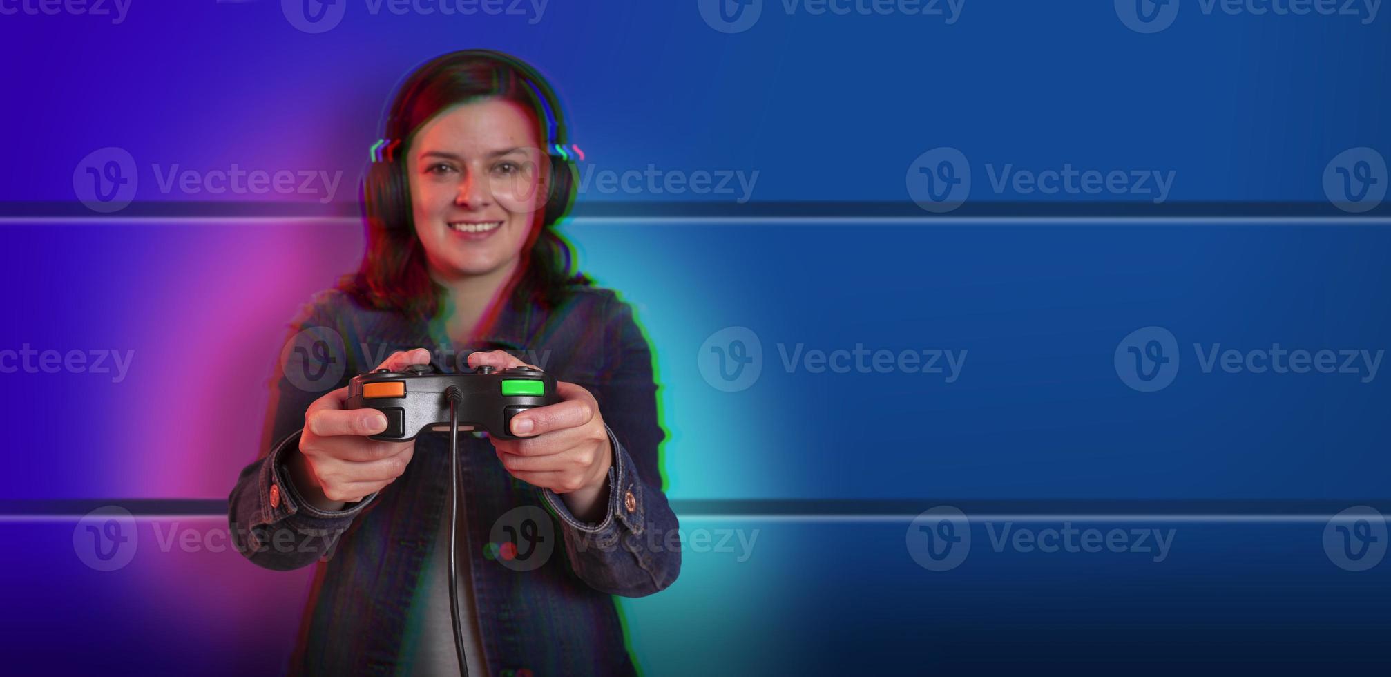 Beautiful young hispanic woman standing front view playing with a video game console in her hands against blue wall background. focus on hands photo