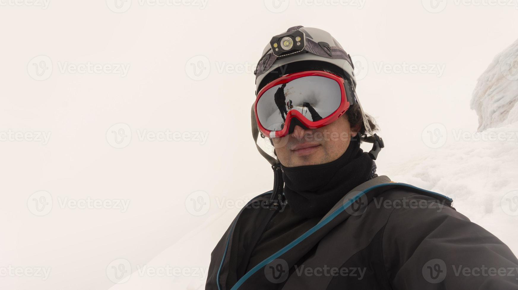 Climber with helmet, headlamp and black jacket taking a selfie on a glacier on a cloudy day photo