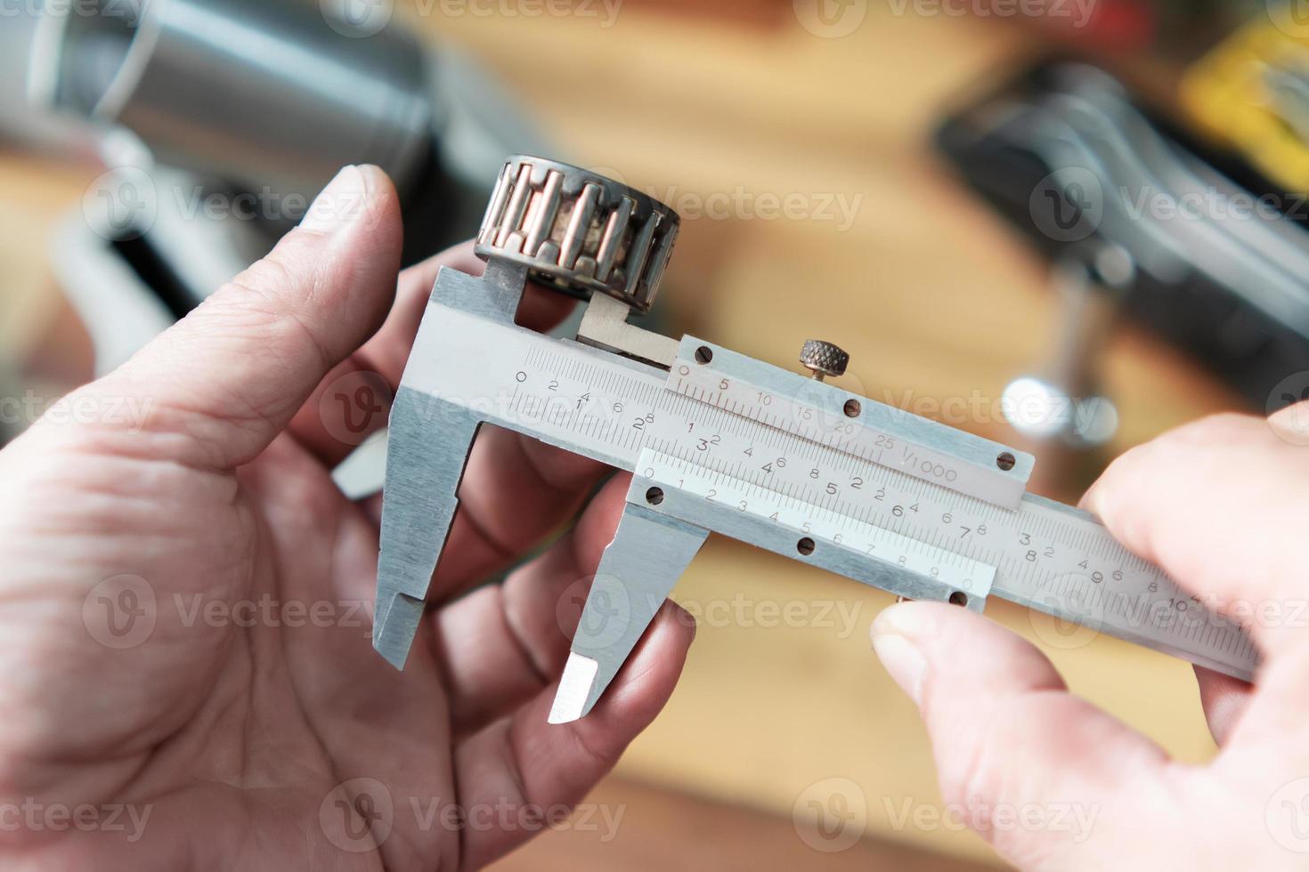 Hand of mechanic holding Vernier Caliper Measurements on needle roller bearing for motorcycle part at motorcycle shop , selective focus on Vernier , photo