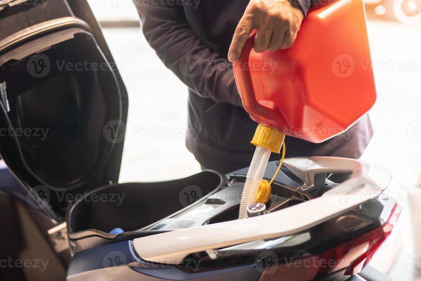 Man fills the fuel into the gas tank of motorcycle  from a red canister or plastic fuel can .maintenance repair motocycle concept ,selective focus photo