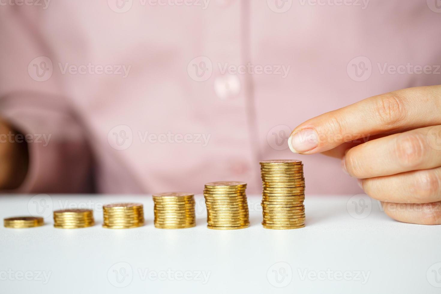 Female hand stacking gold coins into increasing columns photo