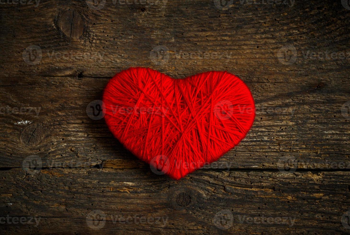 Red heart shape made from wool on old shabby wooden background photo