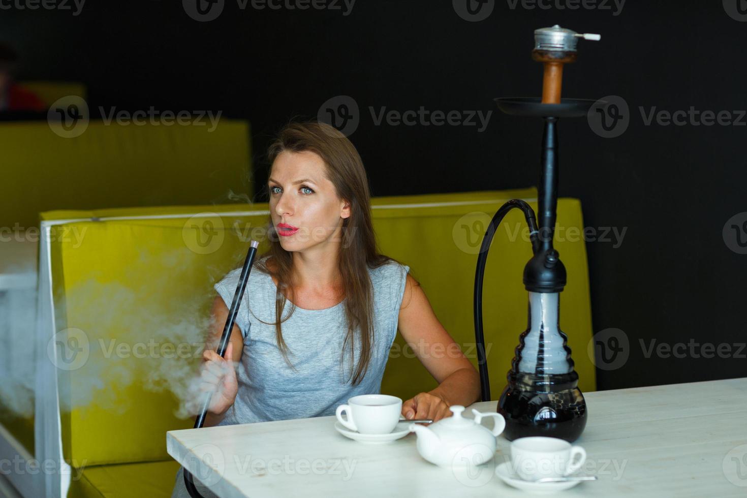 hermosa mujer de fumar un narguile y Bebiendo té en un café foto