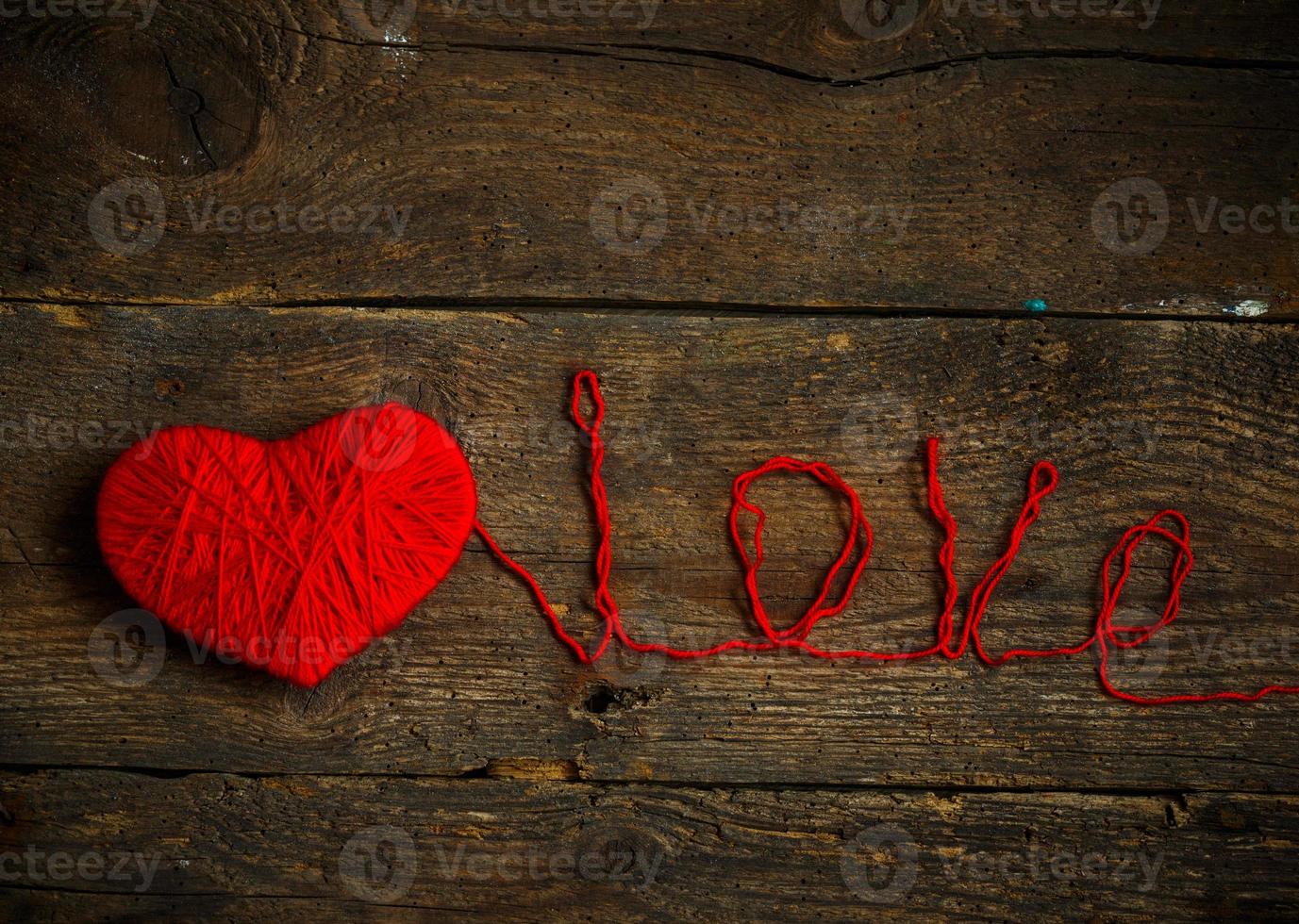 Red heart shape with an inscription love made from wool on old shabby wooden background photo