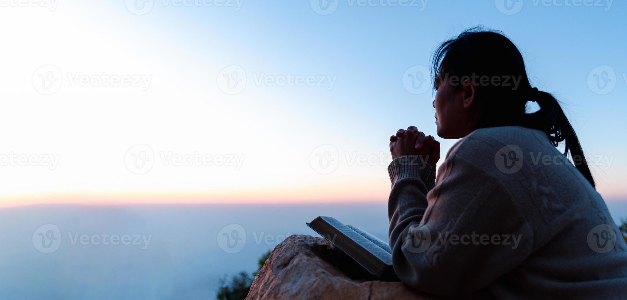 Silhouette of woman kneeling down praying for worship God at sky background. Christians pray to jesus christ for calmness. In morning people got to a quiet place and prayed. Banner with copy space. photo