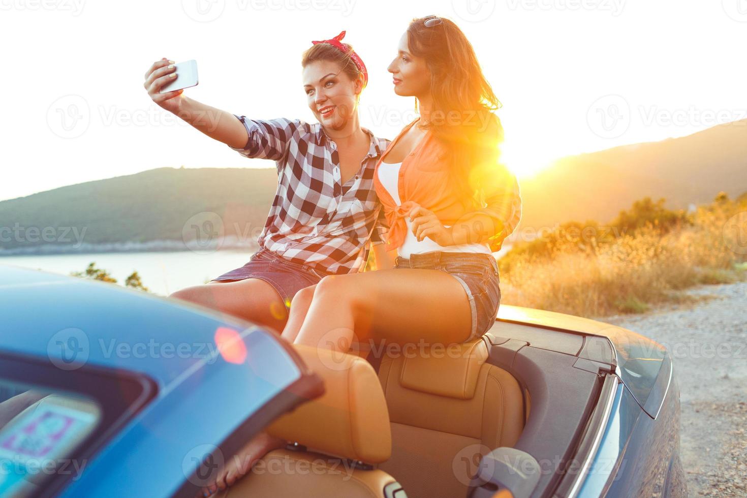 dos joven hermosa muchachas son haciendo selfie en un convertible foto