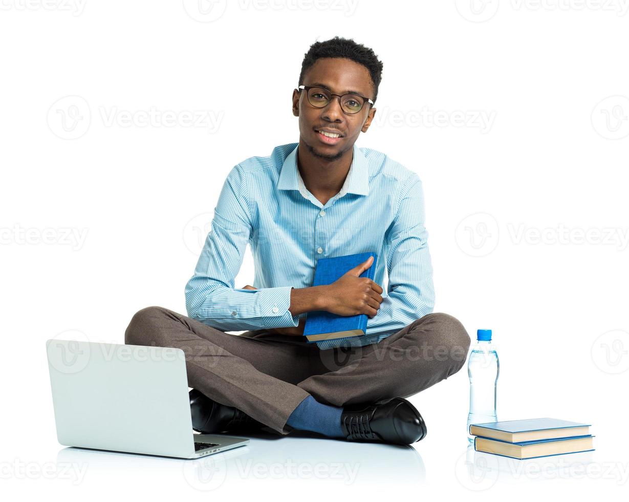 Happy african american college student with laptop, books and bottle of water sitting on white photo