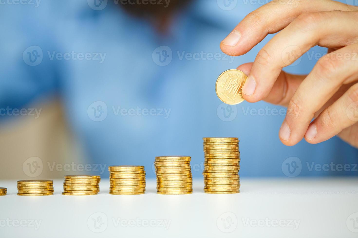 Male hand stacking gold coins into increasing columns photo