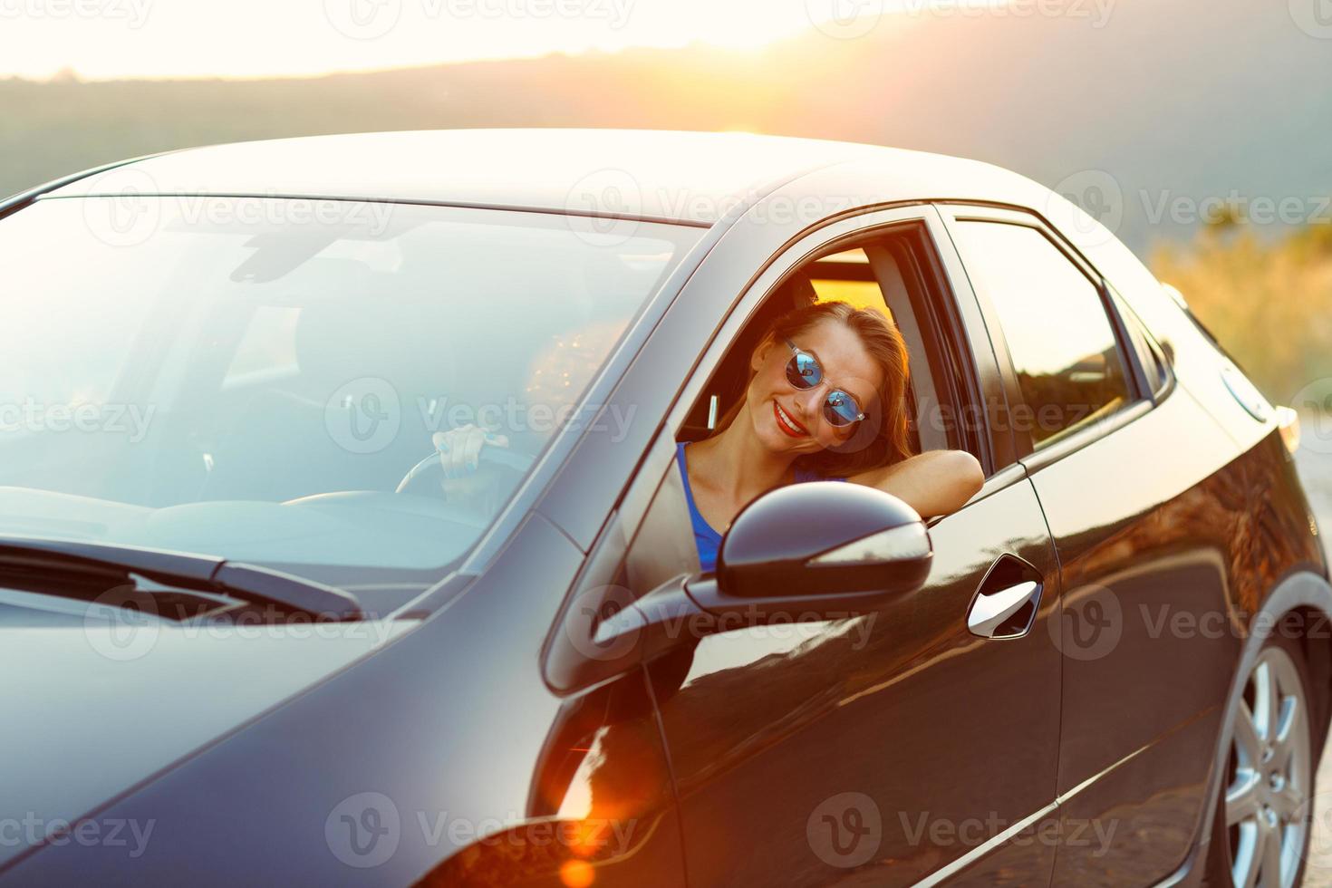 sonriente mujer conducción un coche a puesta de sol foto