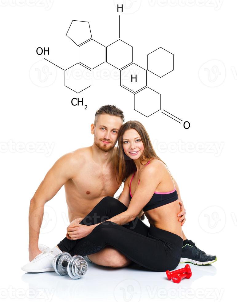 Athletic couple - man and woman after fitness exercise sitting with dumbbells on the white with the chemical formula on background photo