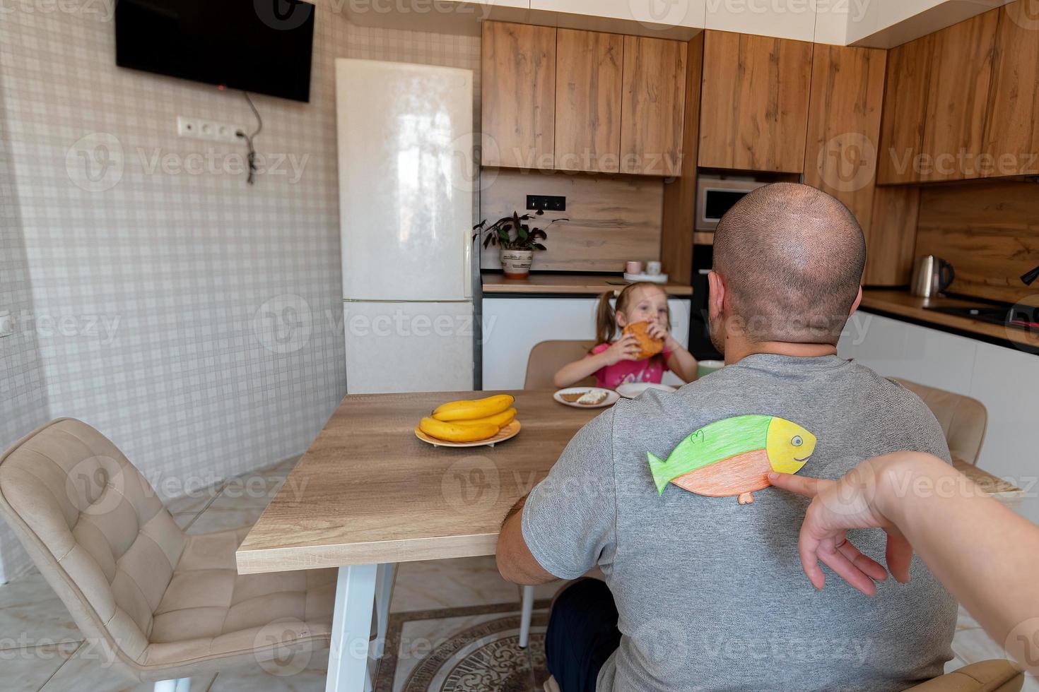 el familia durante desayuno en el cocina en el primero de abril chistes y palos papel pescado en cada otros espaldas gracioso familia chistes, tradiciones, abril tontos día celebracion foto