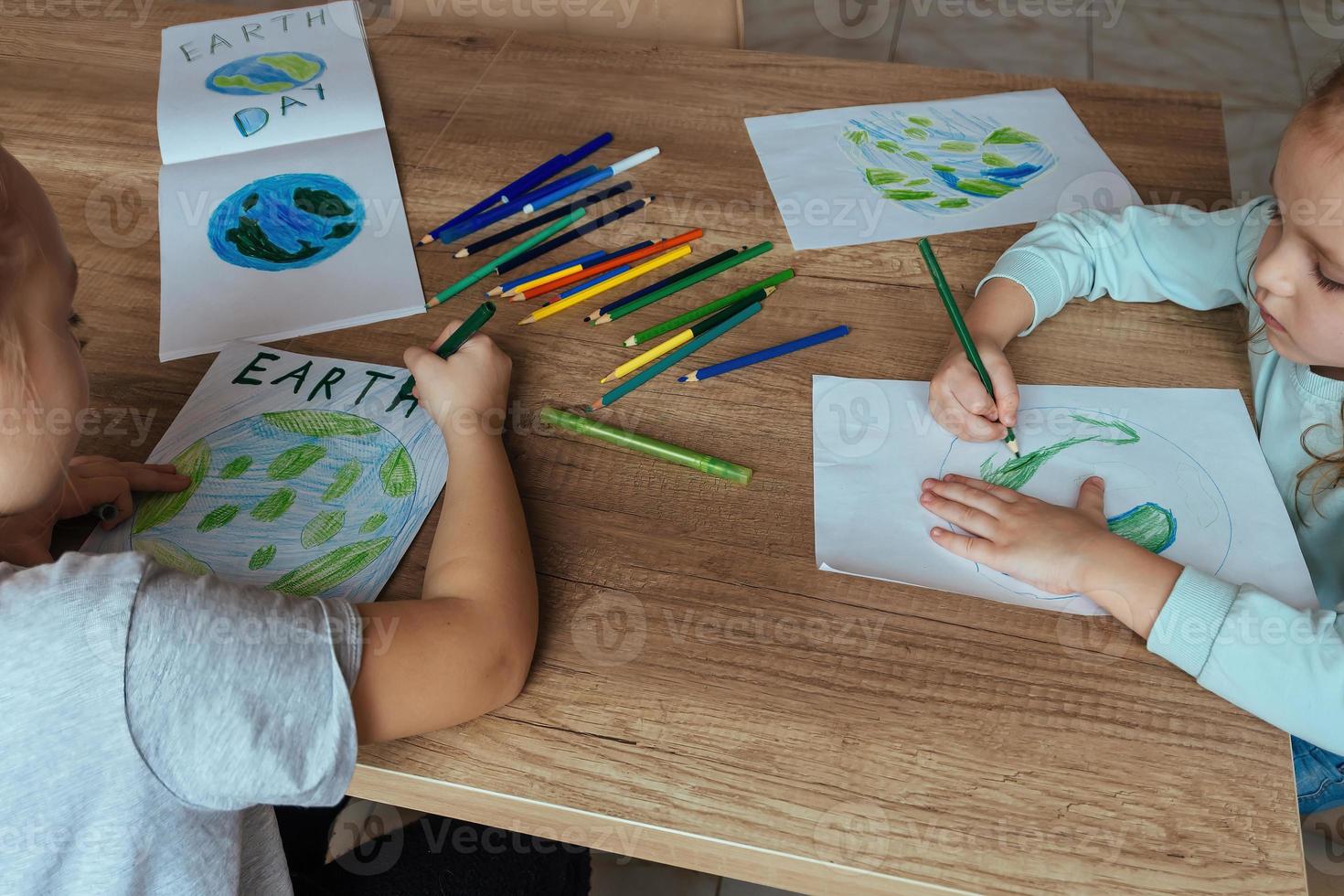 Children draw the planet Earth with pencils and felt-tip pens on album sheets for Earth Day at their home table. photo