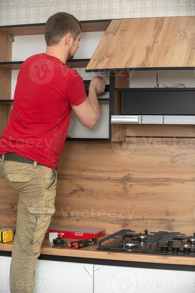 Craftsman, furniture maker and assembler, installs a modern kitchen in the house with tools in hand. Custom furniture concept, home improvement, renovation photo