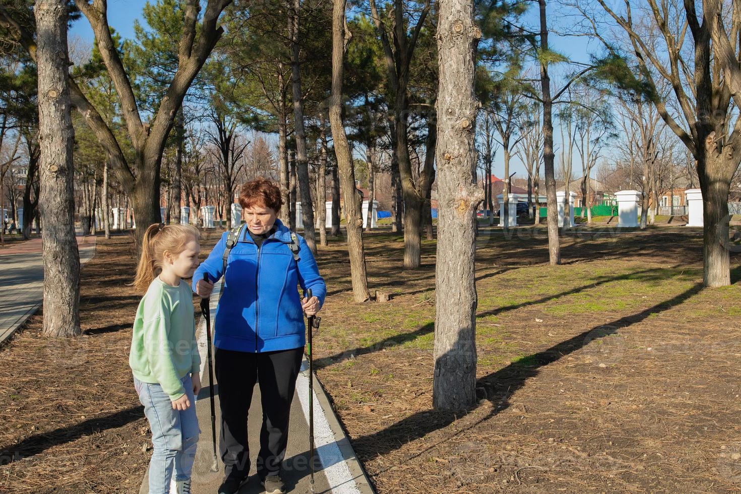 An elderly athletic woman walks in the park on a sunny day with her granddaughter. Care and care in the family for the older generation. photo