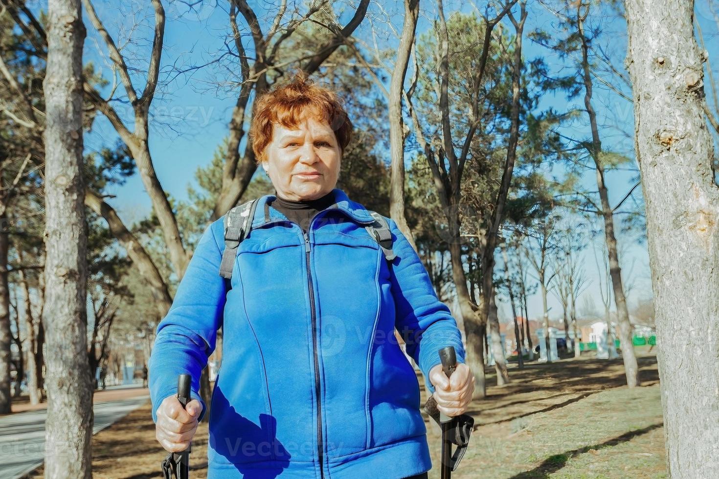 an elderly active woman walks in the park on Scandinavian sticks. Healthy lifestyle of adult women. photo