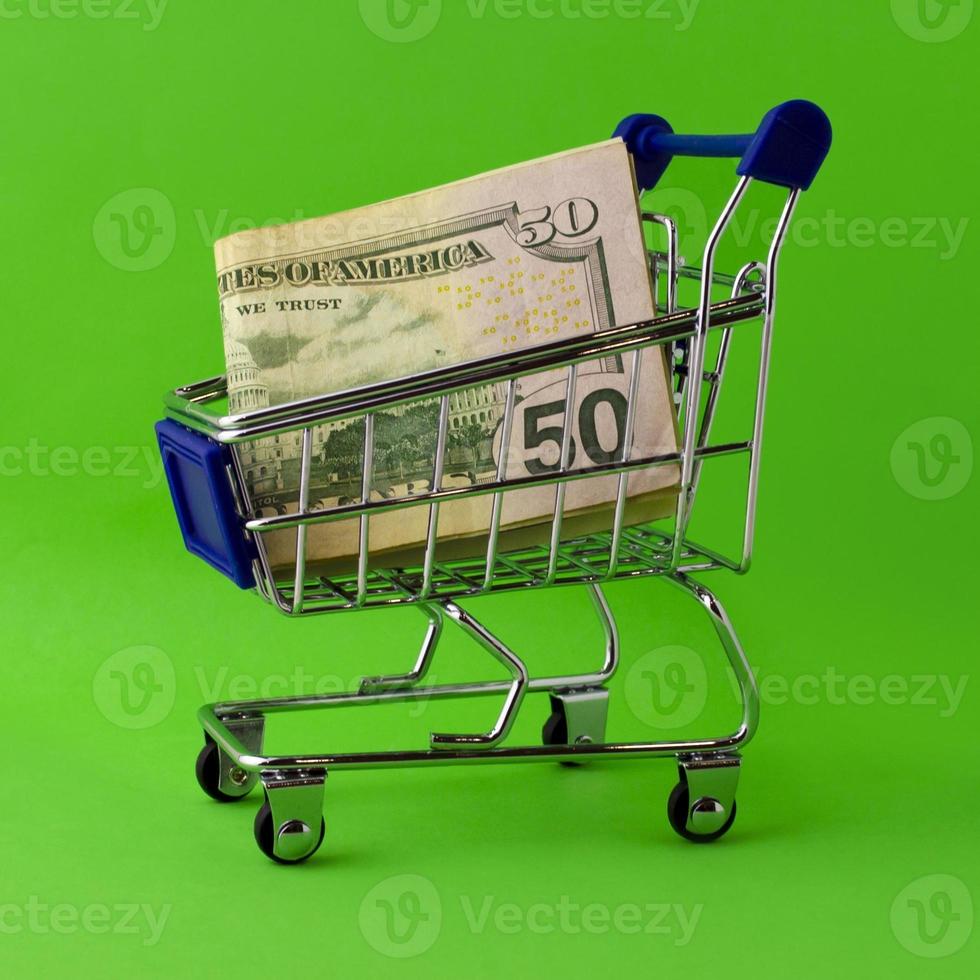 Shopping cart with 50 dollar bills on a green background. photo