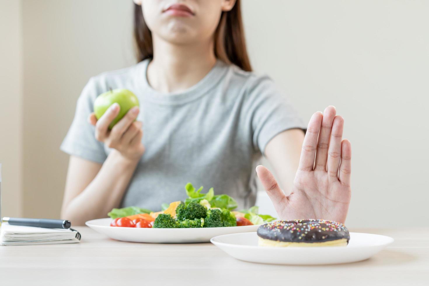 dieta, dieta asiático joven mujer o niña utilizar mano empujar afuera, negar dulce rosquilla y escoger verde ensalada verduras, comer comida para bueno saludable, salud cuando hambriento. cerca arriba hembra peso pérdida persona. foto