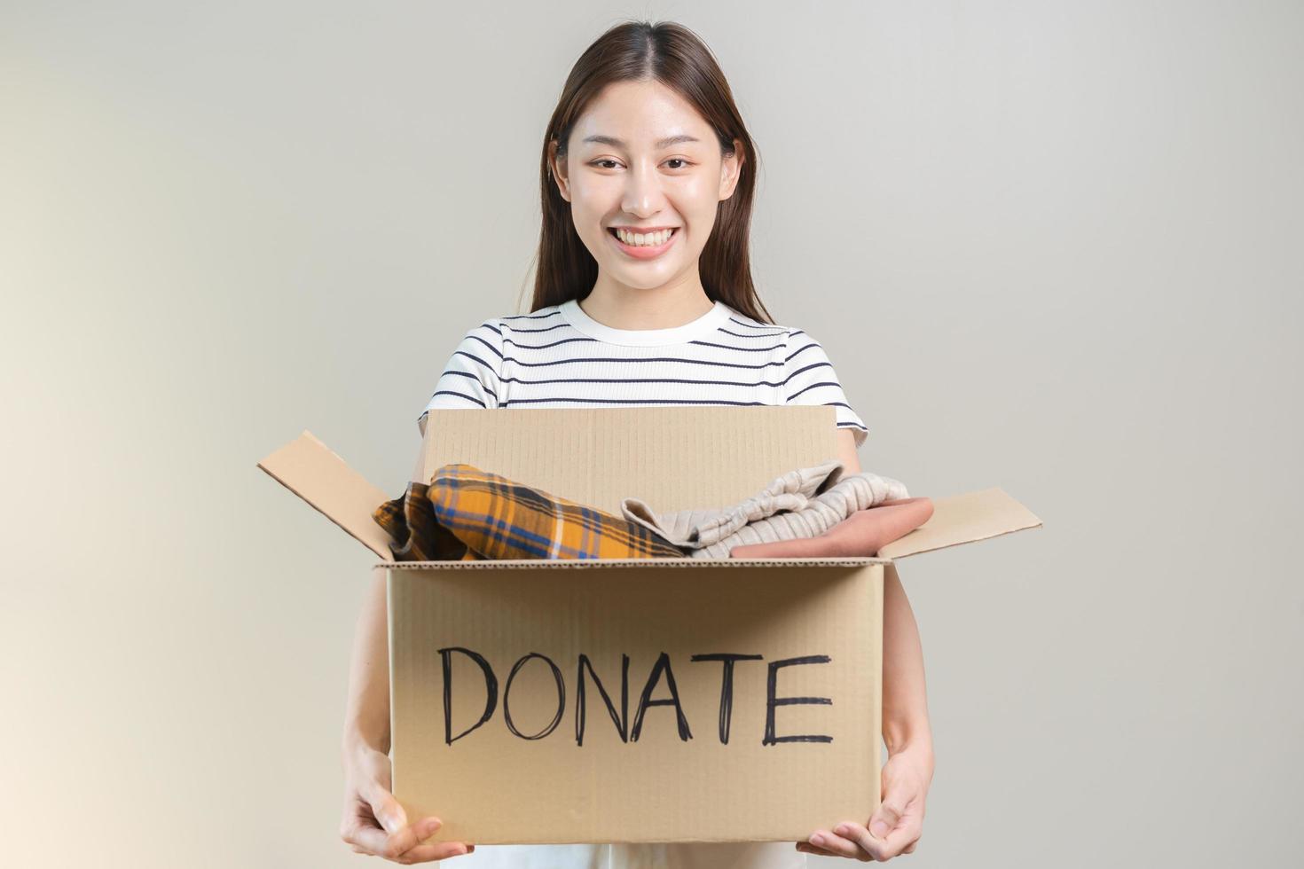 Recycling, Donation for poor, smiling asian young woman pack, holding donate box full with second hand clothes, charity helping and needy people. Reuse recycle, moving of object on white background. photo