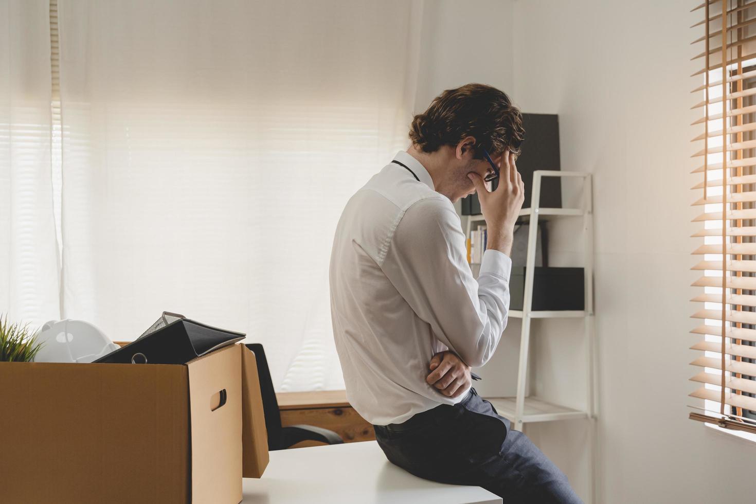 Unemployed, quite job. Desperate caucasian young businessman resigning from company, packing belongings, stuff in box cardboard, layoff or leaving, changing work. Resignation, employment concept. photo