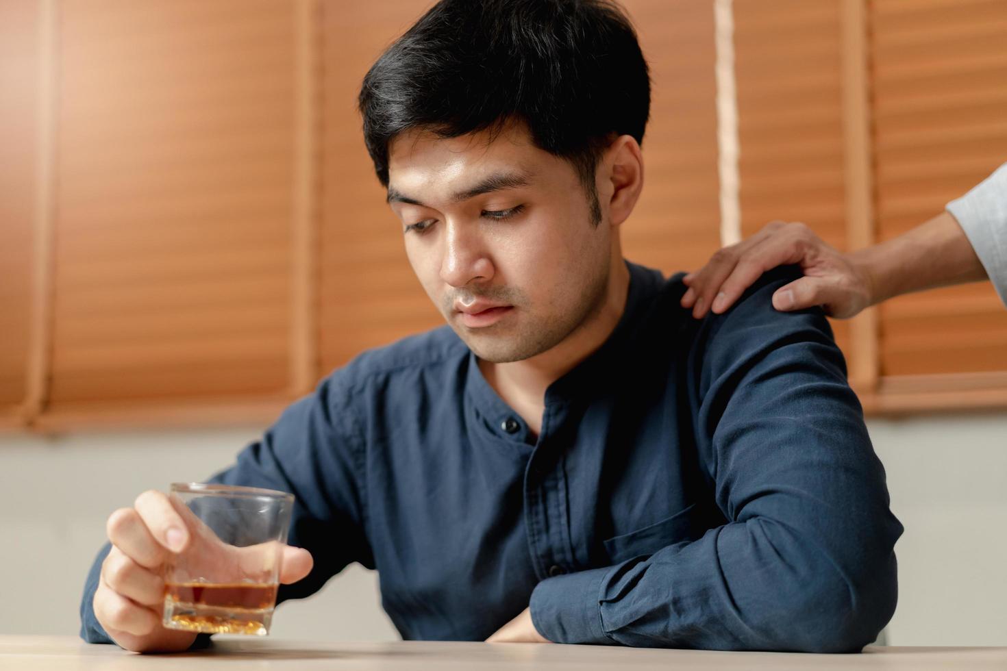 Alcoholism, depressed asian young man sitting on table while drinking alcoholic beverage, holding glass of whiskey at night. Treatment of alcohol addiction, suffer abuse problem alcoholism. photo