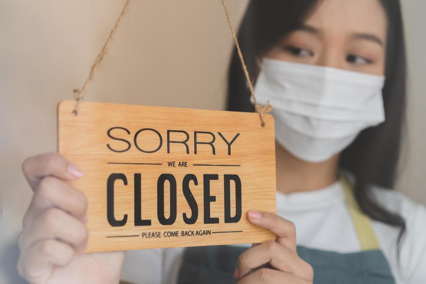 Asian young owner retail,coffee shop woman turning sign board to closed with wearing face mask,protection to pandemic of coronavirus.Close store,restaurant or pub due to lockdown, quarantine of covid. photo