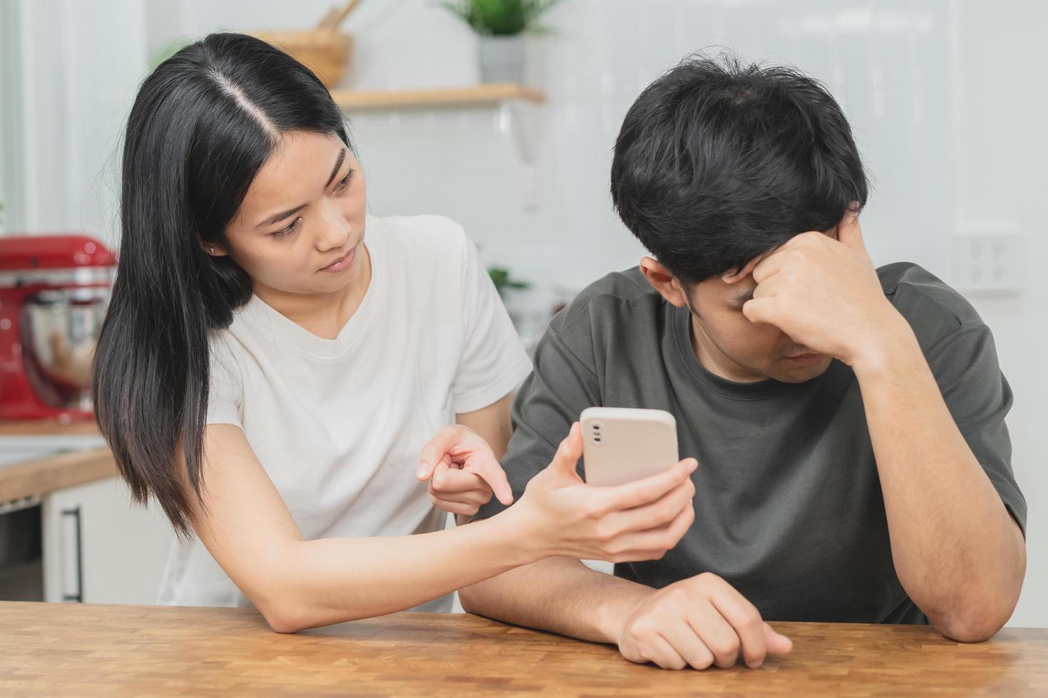 Infidelity, suspicion asian young couple love fight relationship, wife holding cellphone, smartphone cheating on phone, scolding husband about mistrust, distrust and jealousy when sitting at home. photo