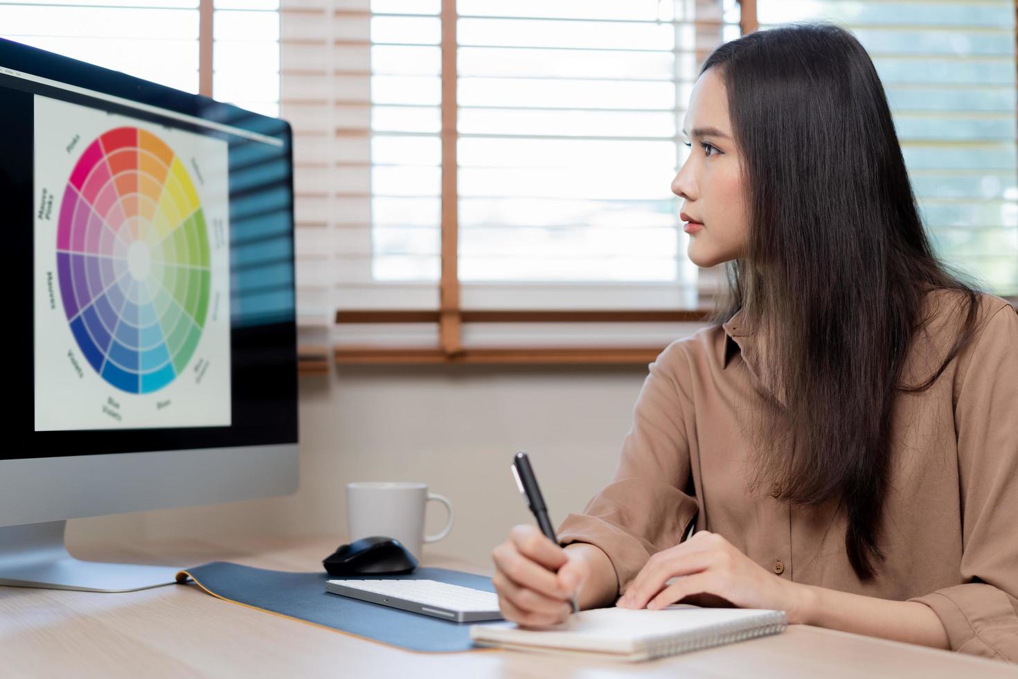 Video meeting conference via camera, Beautiful asian young business woman looking on screen web, using PC computer, making notes, sitting in home office, freelancer working.Technology, social distance photo